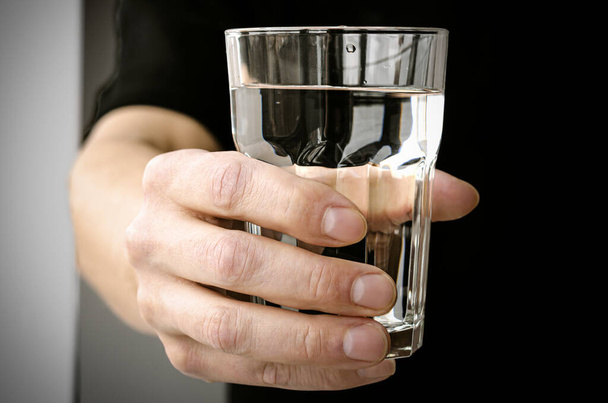 Mano con un vaso de agua pura de manantial sobre fondo negro - Foto, Imagen