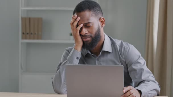 Anxious stressed tired young African American male employee manager or black student sitting with laptop falls asleep guy overwhelmed working on computer at modern home office, chronic fatigue concept - Footage, Video