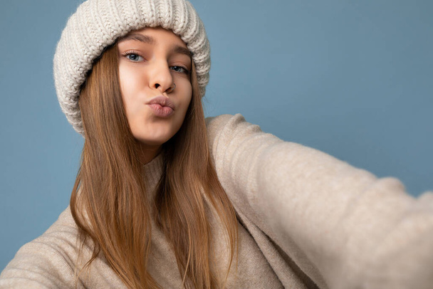 Closeup shot of beautiful sexy positive young dark blonde woman isolated over colourful background wearing everyday trendy clothes looking at camera and giving kiss, concept of selfie photo - 写真・画像
