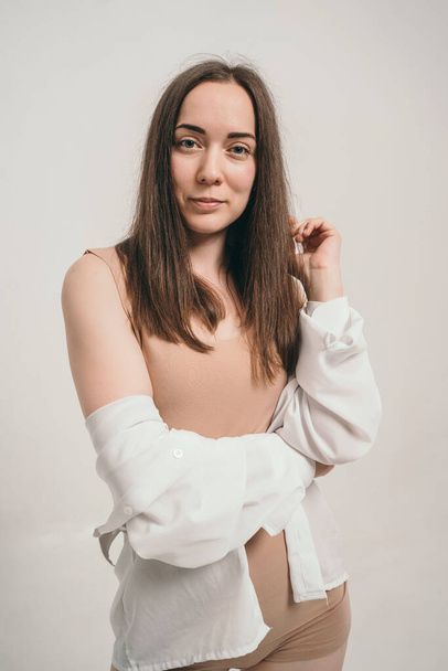 Portrait of a beautiful girl in a white shirt. Cute brunette looks into the frame. A brave and sweet girl in the frame. The natural beauty of the girl is in the light. - Foto, afbeelding