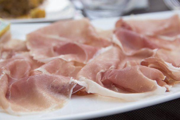 Prosciutto, een Italiaanse gedroogde ham, dun gesneden en ongekookt geserveerd in een witte plaat - Foto, afbeelding