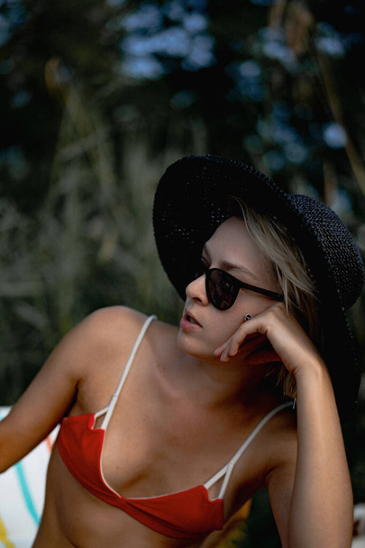 young beautiful woman in a black straw hat and red swimsuit on lounger - Fotoğraf, Görsel