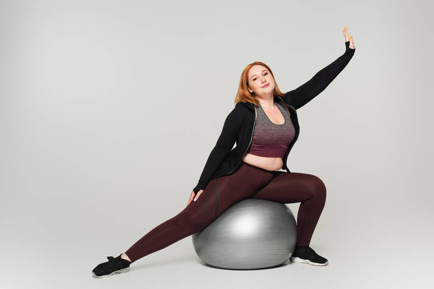 Plus size sportswoman exercising on fitness ball on grey background - Fotoğraf, Görsel