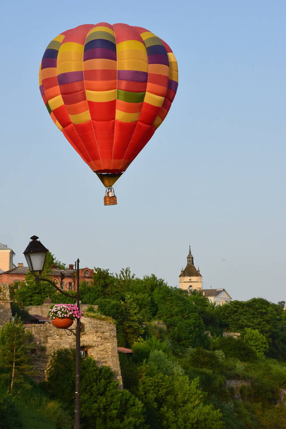大規模な多色熱気球は、古代の建物や密生した木の谷の上を低飛行します。至近距離から撮影 - 写真・画像