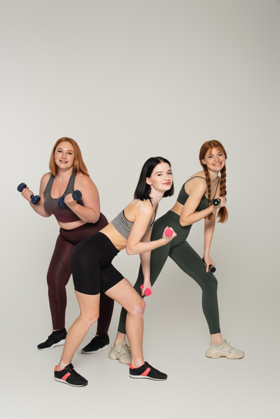 Body positive women exercising with dumbbells on grey background - Foto, imagen