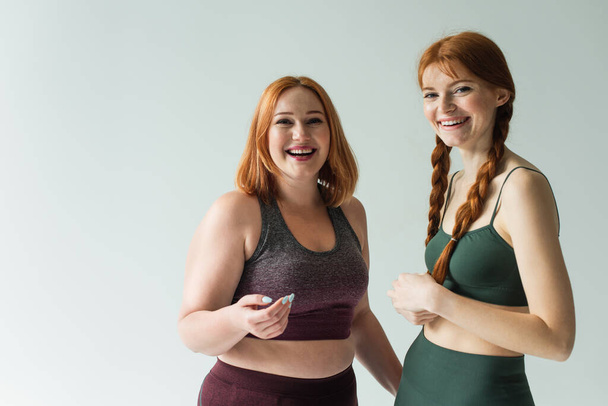 Smiling body positive sportswomen looking at camera isolated on grey  - Fotoğraf, Görsel