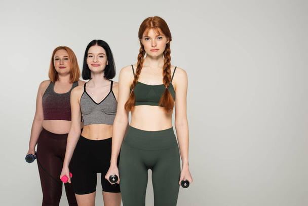 Szürkén izolált súlyzókat tartó testpozitív sportnők  - Fotó, kép