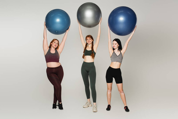 Body positive sportswomen holding fitness balls on grey background - 写真・画像