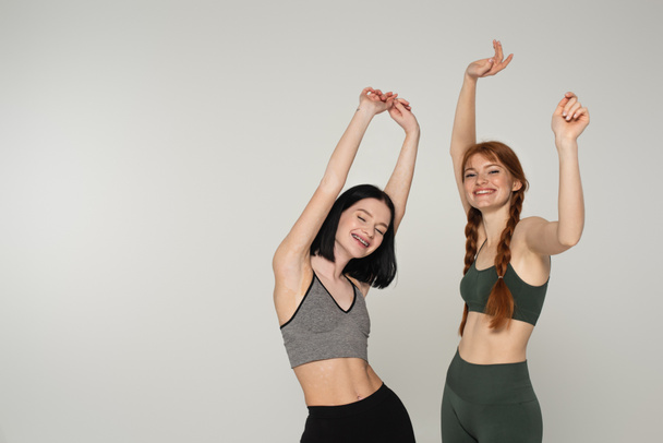 Hübsche körperlich positive Sportlerinnen tanzen isoliert auf grau  - Foto, Bild