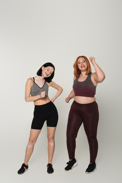 Body positive friends in sportswear dancing on grey background  - Photo, Image
