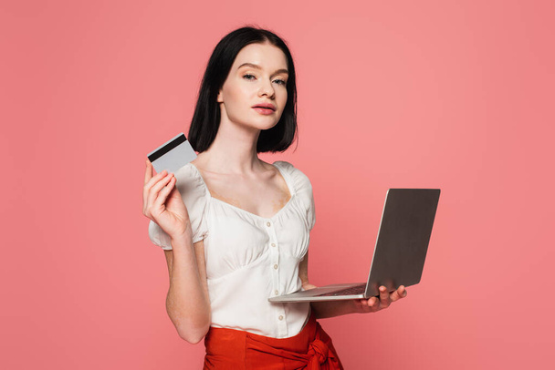 Woman with vitiligo holding credit card and laptop isolated on pink  - Photo, Image