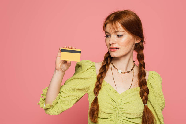 Freckled woman looking at credit card isolated on pink  - Foto, afbeelding