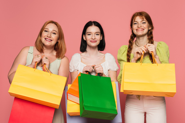 Smiling woman with vitiligo holding shopping bags near body positive friends on pink background  - Photo, Image