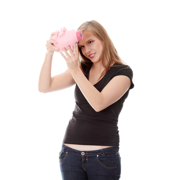 νεαρή γυναίκα που προσπαθεί να πάρει χρήματα από την Τράπεζα γουρουνάκι, απομονώνονται σε λευκό φόντο - Φωτογραφία, εικόνα