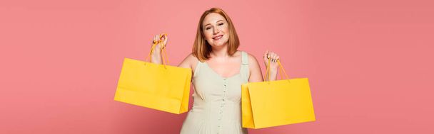 Smiling plus size woman holding shopping bags isolated on pink, banner  - Photo, Image