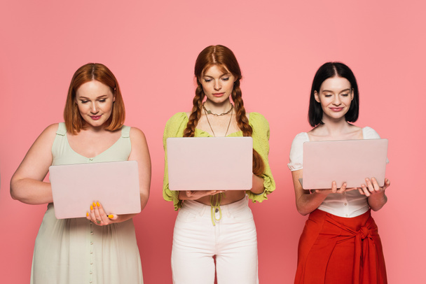 Гарне тіло позитивні жінки використовують ноутбуки ізольовані на рожевому
  - Фото, зображення