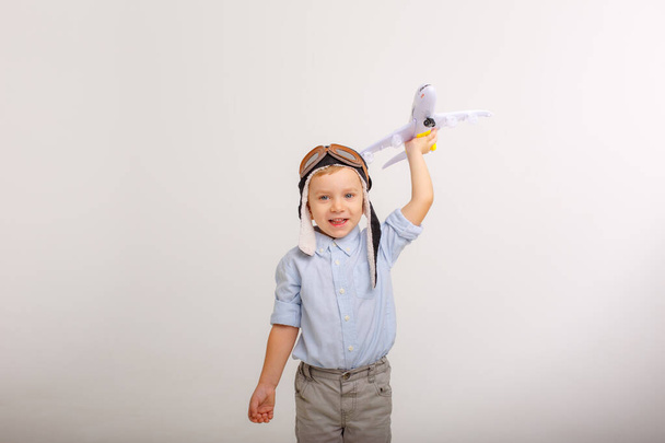 een jongetje met een pilotenmuts en een vliegtuig op een witte achtergrond - Foto, afbeelding
