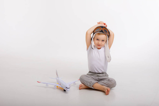 Pilot şapkalı küçük bir çocuk ve beyaz bir arka planı olan bir uçak. - Fotoğraf, Görsel