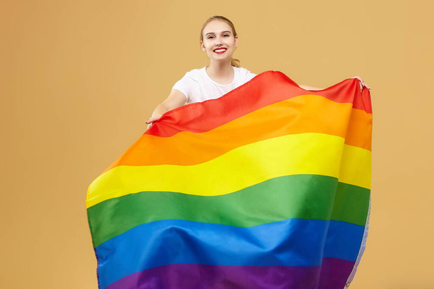 attractive blonde made posing with a rainbow LGBT flag. photo shoot in the studio on a yellow background. - 写真・画像