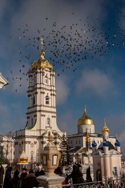 Manada de palomas vuela sobre el campanario, la Catedral de la Trinidad y el complejo del monasterio de la Santa Dormición Pochayiv Lavra, Pochayiv, Ucrania. Enero de 2009 - Foto, imagen