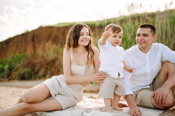 Cheerful young family with little baby boy spending time together on the beach. Father, mother and child against the background of the blue sea and sky. Family, childhood, active lifestyle concept. - Foto, afbeelding