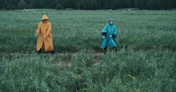 Man in gele regenjas en een vrouw in blauwe regenjas dansen in een veld - Video