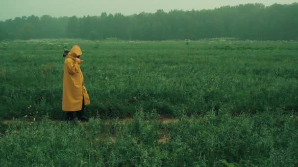 Maniak w żółtym płaszczu rzuca siekierą w uciekającą kobietę w niebieskim płaszczu przeciwdeszczowym - Materiał filmowy, wideo