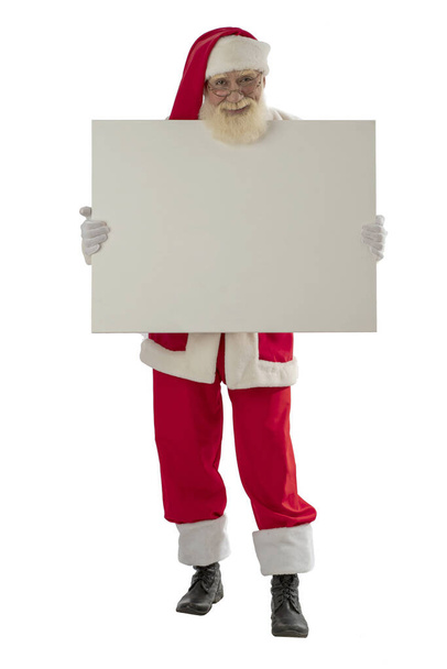 Santa Claus on white background isolated. Senior actor old man with a real white beard in the role of Father Christmas holding a mock up board. Male character stands upright full-length - Fotó, kép
