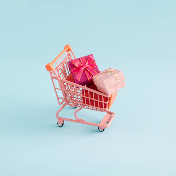 Gifts in the pink shopping cart on blue background. Creative minimal concept. - Photo, Image