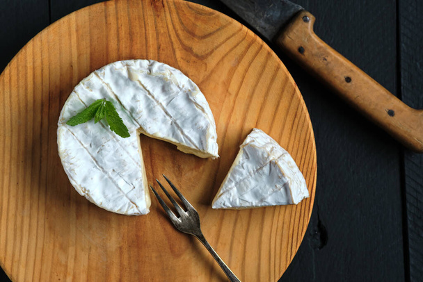 Shot from above of piece of creamy camembert cheese with some mint leaves on wooden board - Zdjęcie, obraz