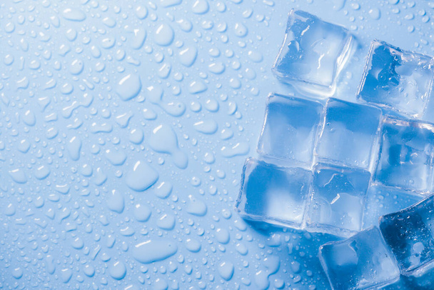 macro vista foto di cubetti di ghiaccio e gocce d'acqua su sfondo blu con copia spazio vuoto. Cubi di ghiaccio con gocce d'acqua sparse su fondo blu - Foto, immagini