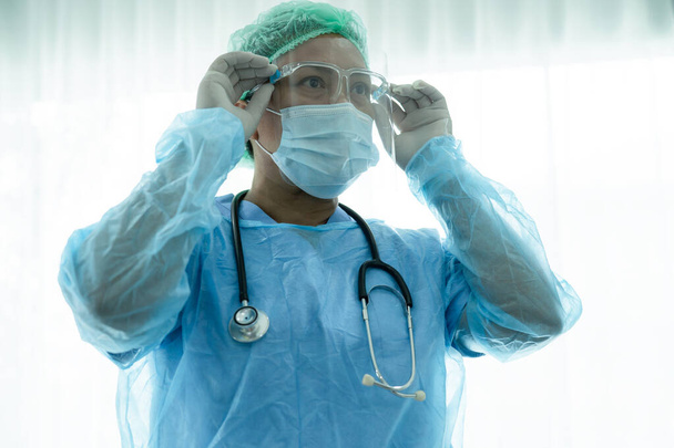 Azjatycki lekarz noszący osłonę twarzy i kombinezon ochronny nowy normalny w celu sprawdzenia bezpieczeństwa pacjenta Covid 19 Epidemia koronawirusa na oddziale kwarantanny w szpitalu pielęgniarskim. - Zdjęcie, obraz