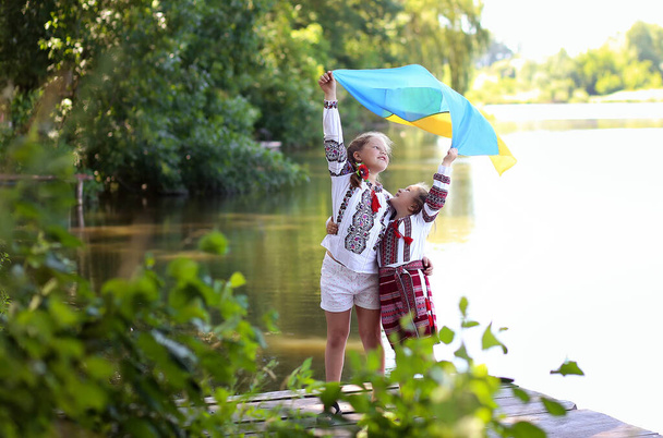 Lányok testvér barátok hímzett nemzeti ukrán jelmezek sárga-kék zászlót a mólón a tó partján. Függetlenség napja Ukrajna, alkotmány, Vyshyvanka nap, zászló nap - Fotó, kép