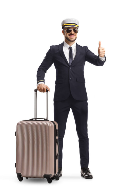 Full length portrait of a young handsome pilot with a suitcase gesturing a thumb up sign isolated on white background - Valokuva, kuva