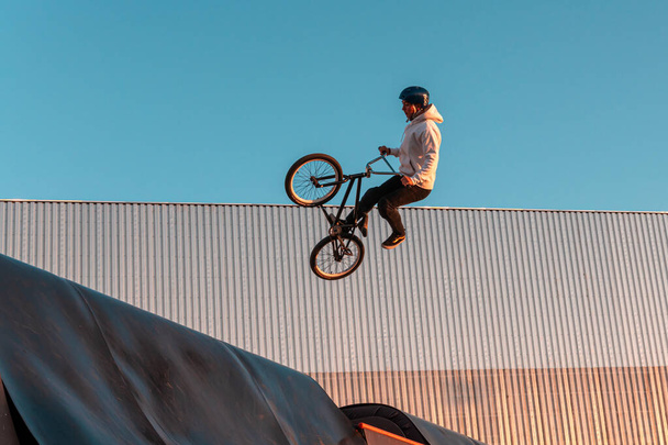 A BMX rider does a stunt on a ramp in a skate park in the city public park for outdoor activities - Fotografie, Obrázek