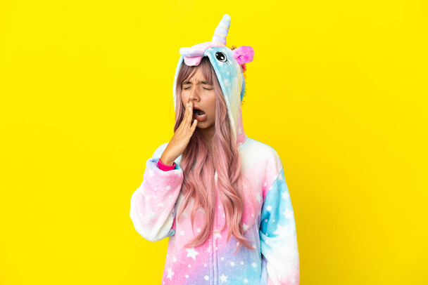 Young mixed race woman wearing a unicorn pajama isolated on white background yawning and covering wide open mouth with hand - Photo, Image