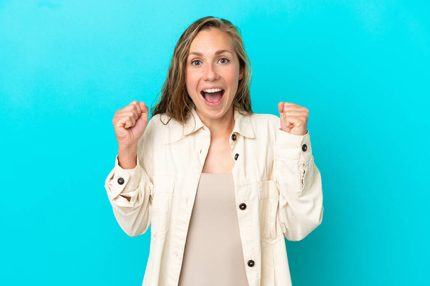 Young caucasian woman isolated on blue background celebrating a victory in winner position - Photo, Image