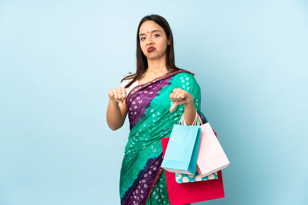 Mulher indiana jovem com sacos de compras mostrando polegar para baixo com duas mãos - Foto, Imagem