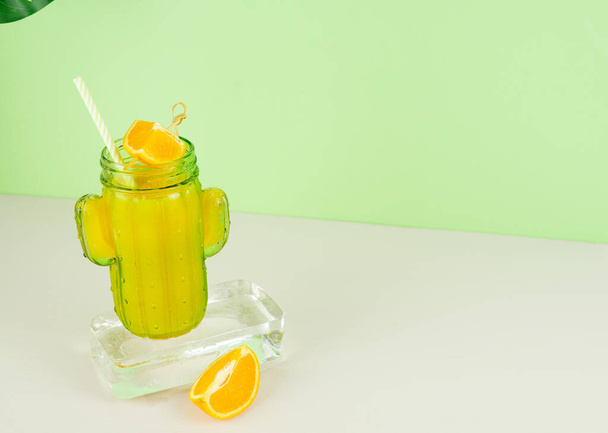 Orange juice in cactus shaped glass on ice block with fruit decoration. Copy space. - Photo, Image