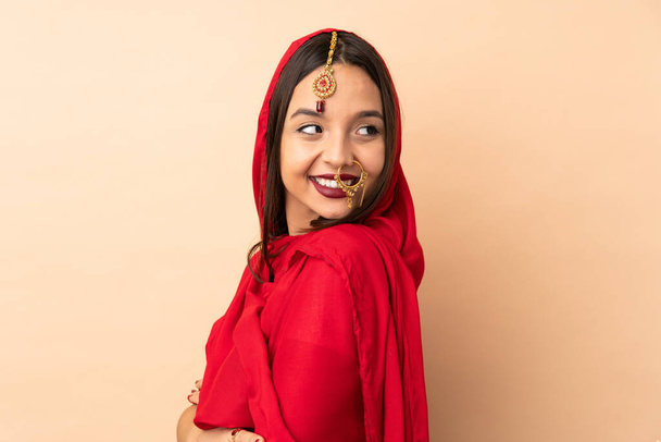 Young Indian woman isolated on beige background with arms crossed and happy - Foto, afbeelding