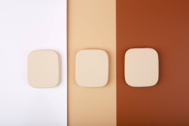 Creative flat lay with three square shaped make up sponges on white, beige and brown background. Concept of make up for all skin tones from light to dark - Fotó, kép