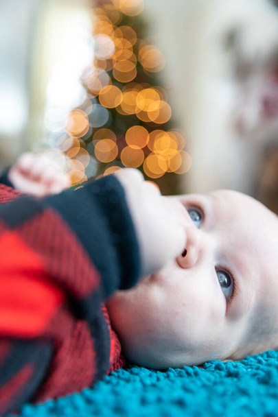 Baby's first Christmas laying on floor near tree.  - Foto, Bild