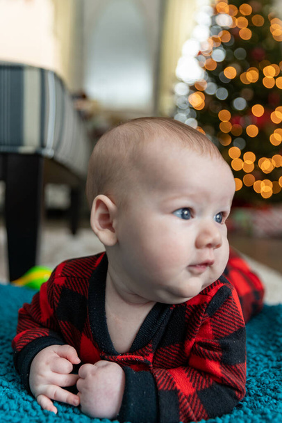 赤ちゃんの最初のクリスマスは木の近くの床に寝そべって.  - 写真・画像
