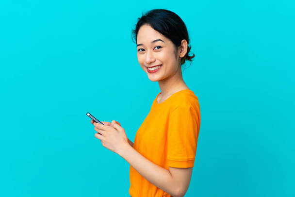 Jeune femme vietnamienne isolée sur fond bleu envoyer un message ou un courriel avec le mobile - Photo, image