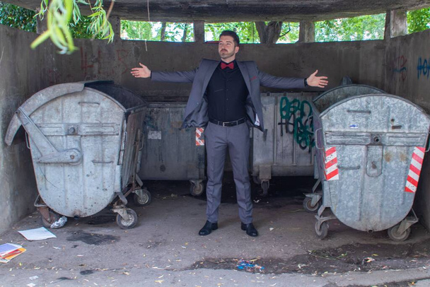 Парень в костюме и бабочке позирует перед мусорными баками - Фото, изображение