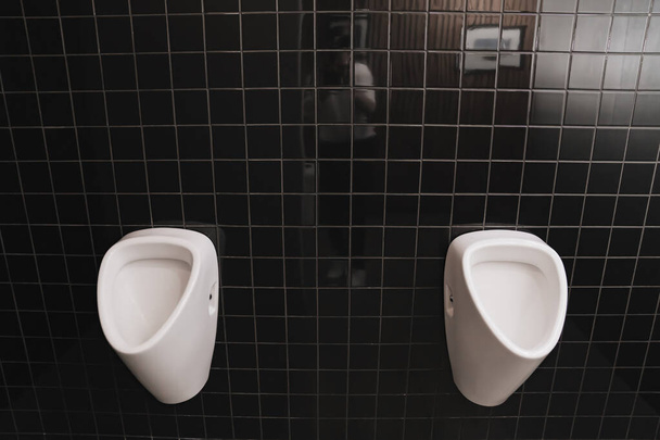 mens toilet with urinal. toilet room with black ceramic tiles on the walls.  - Фото, изображение