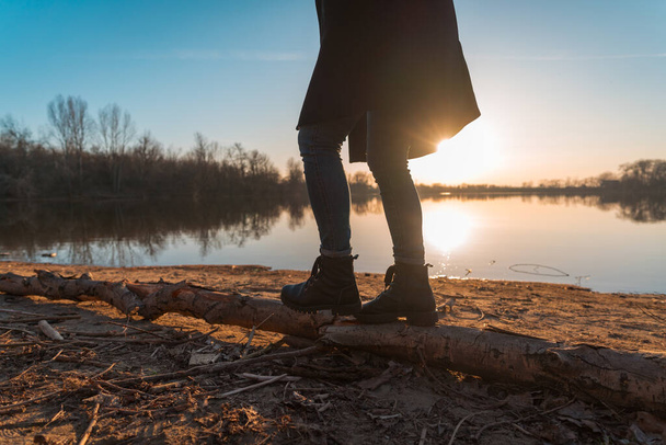 Nuori tyttö kävelee tukin rannalla järven ja auringonlaskun taustalla - Valokuva, kuva