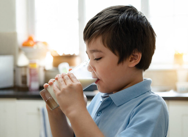 Portrait healthy school boy drinking glass of milk for breakfast, Happy child standing in kitchen drinking warm milk before go to school. Healhty food liftstyle concept - Photo, image