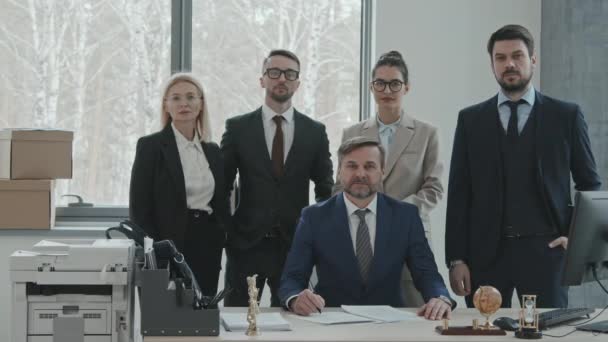 Modern ofisteki iş yerinde kameraya poz veren takım elbiseli beş kendinden emin erkek ve kadın avukatın orta yavaş portresi. - Video, Çekim