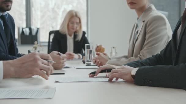 PAN midsection slowmo shot dwóch biznesmenów podpisujących kontrakt i uścisk dłoni siedzących przy stole negocjacyjnym podczas gdy ich prawnicy kontrolują proces - Materiał filmowy, wideo